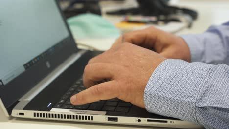 face mask on desk next to male fingers typing on keyboard