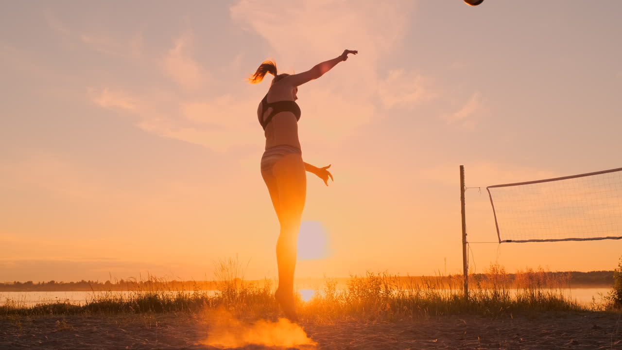 Athletic girl playing beach volleyball jumps in the air and strikes the ball over the net on a beautiful summer evening. Caucasian woman score a point.