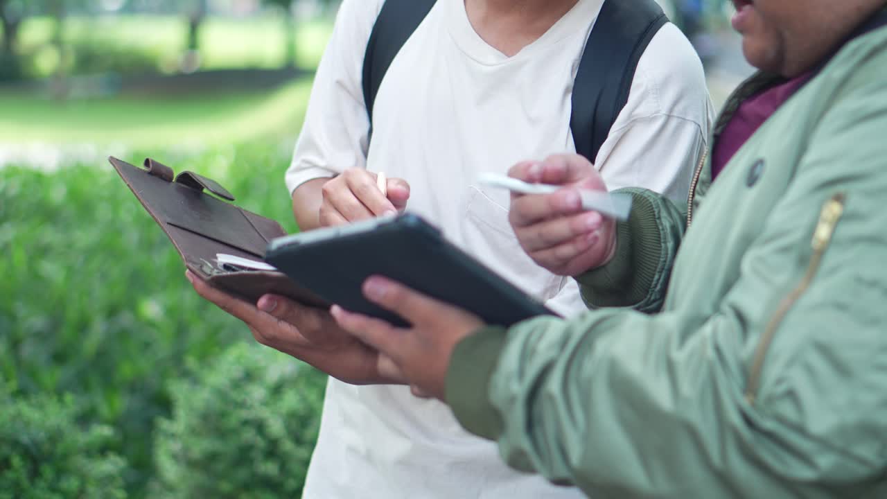 Hands Of Two Young Asian College Students Studying Using Tablet And Writing On Notebook