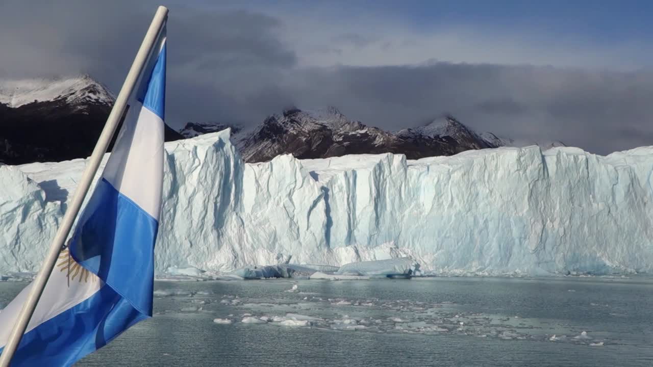 Argentinian flag waving near Perito Moreno Glacier, ice wall and snowy peaks in background