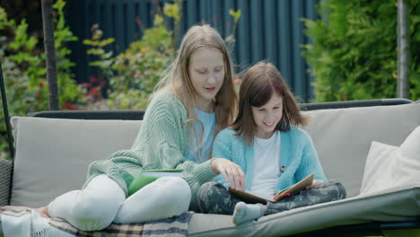 two girls read books, sit on a garden swing in the backyard of the house