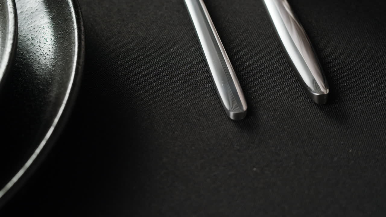 Minimalist table setting with white plate, fork, and knife arranged neatly, and a gloved hand adjusting cutlery.