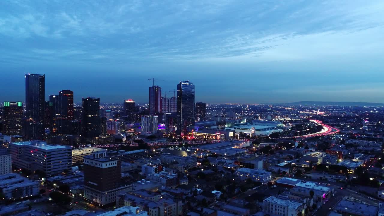 Backward drone flight over Los Angeles during dusk - vibrant skyline city lights