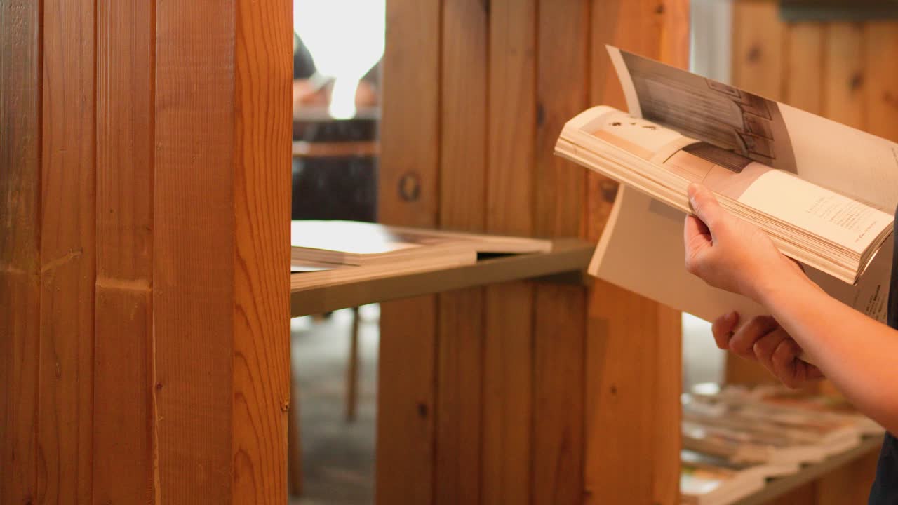Nahaufnahme von Händen, die in einem warmen Restaurant oder einer Bibliothek aus Holz in einer Zeitschrift blättern