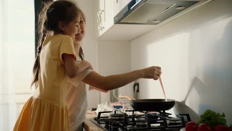 A-little-brunette-girl-in-a-yellow-dress-communicates-with-her-mother-while-she-prepares-breakfast-in-the-morning-in-the-kitchen