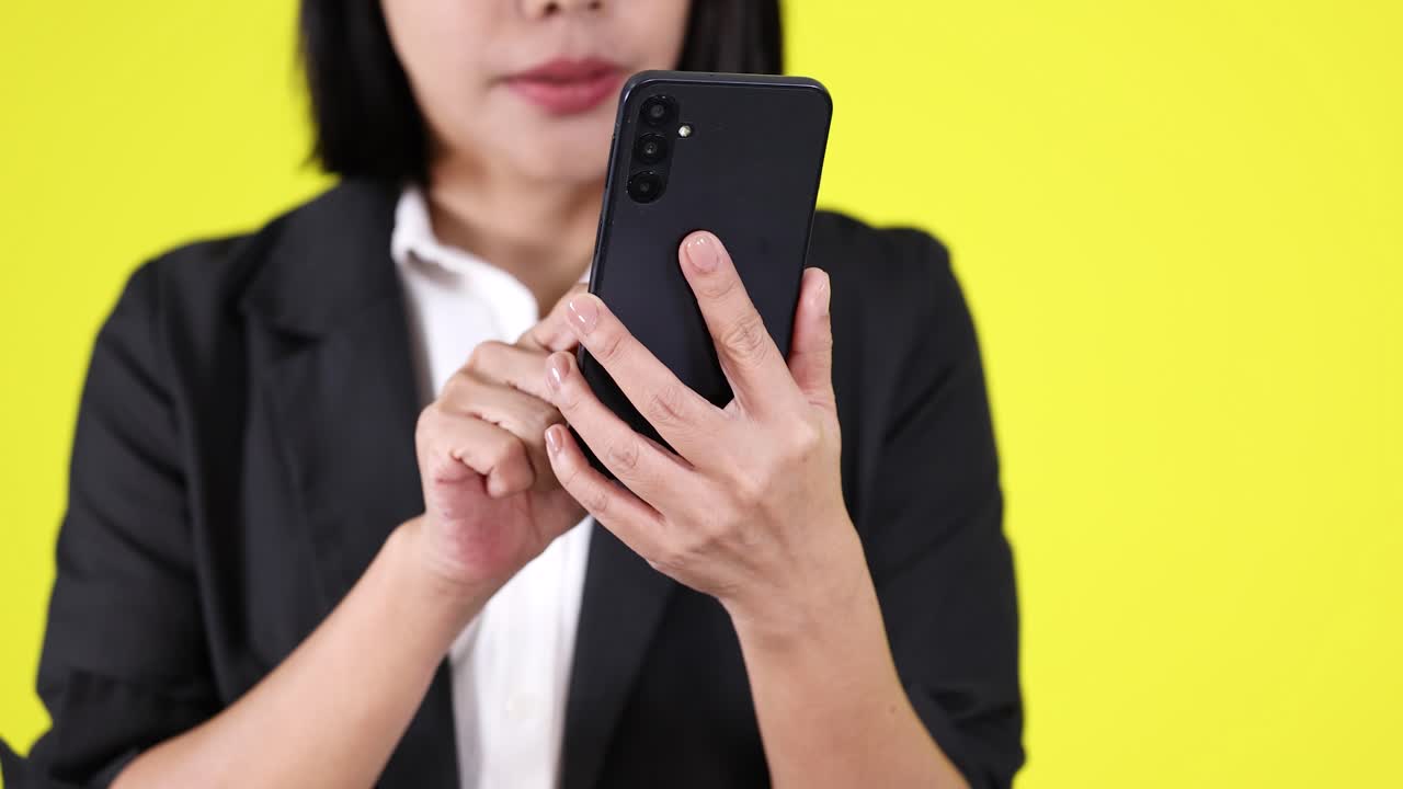 Woman in black blazer using smartphone, mid-shot, vibrant yellow backdrop, even studio lighting