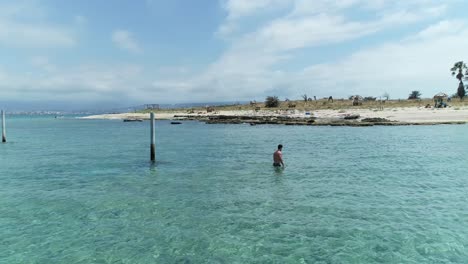 Drone-view-of-palm-Island-beach-with-young-man-walking-to-shore,-circle-pan,-day