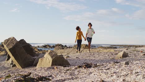 pareja afroamericana cogida de las manos caminando por las rocas cerca del mar