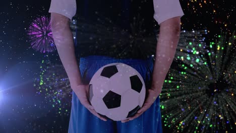 Animation-of-fireworks-over-back-view-of-caucasian-male-soccer-player-holding-ball