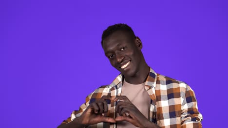 Happy-black-man-in-plaid-shirt-showing-heart-sign-hands,-charity-gesture,-love.-Handmade-heart-gesture.-Smiling-over-blue-background