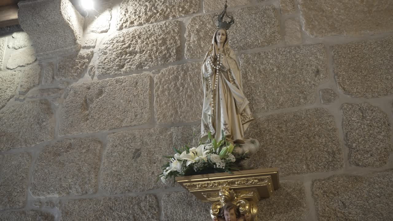 Statue of Virgin Mary with rosary on golden bracket against rough stone church wall