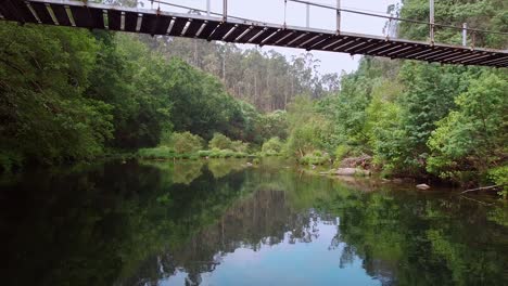 Toma-Aérea-Bajo-Un-Puente-Peatonal-De-Madera-Sobre-El-Río-Verdugo,-Soutomaior-En-Galicia,-España