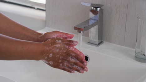 Close-up-of-african-american-woman-washing-her-hands-in-the-bathroom-sink-at-home