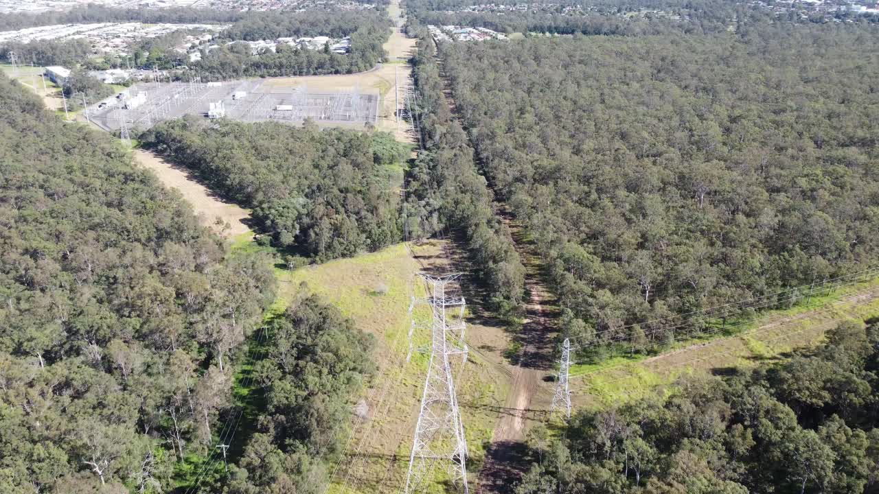 Drone flying over high voltage powerlines towards a suburb with homes in Australia