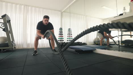 joven usando cuerdas de batalla para un ejercicio rápido de azotes en un gimnasio