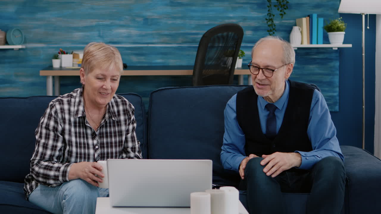 Happy senior couple waving at videocall with nephews using laptop