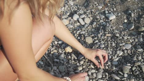 A young, white girl picks up rocks on a beach