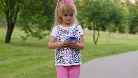 Child-girl-holding-colorful-squishy-silicone-bubbles-sensory-pop-it-toy-game-while-walking-in-park