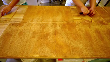hands preparing dough sheets in a bakery, showcasing teamwork and skill
