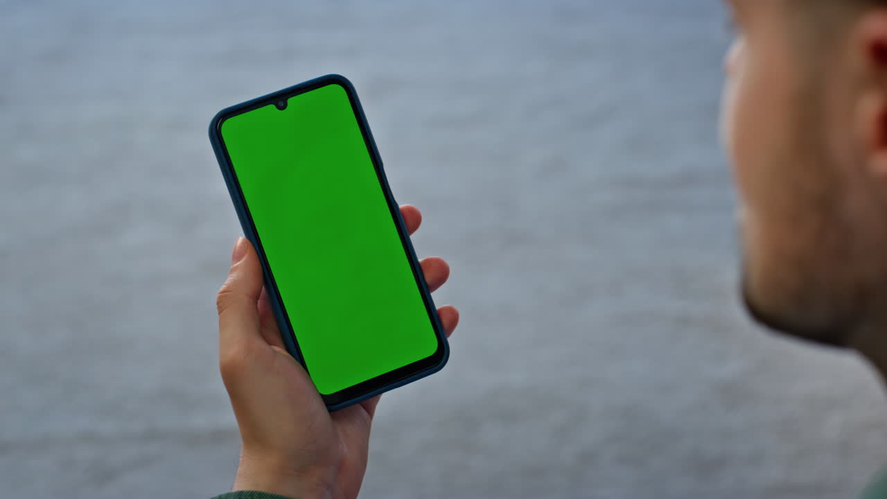 Smartphone user watching green screen room closeup. Man hand holding cellphone
