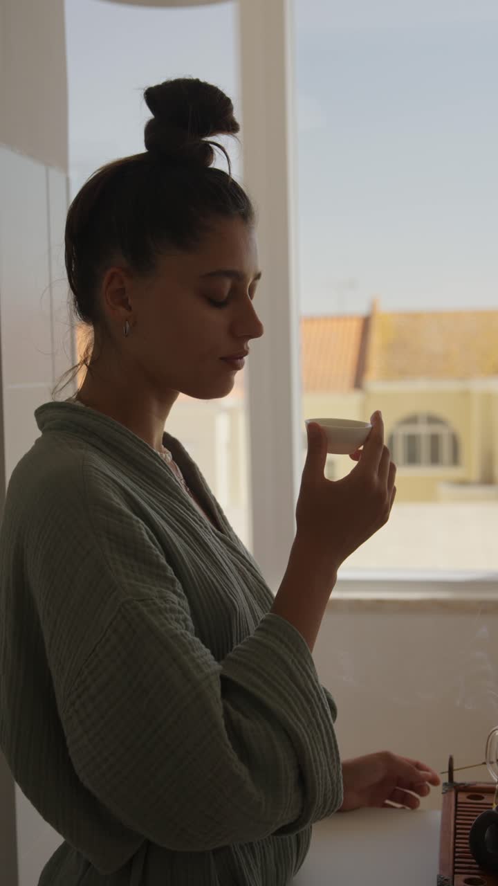 Woman enjoying tea in robe near window