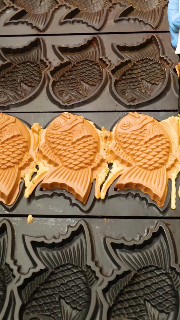 Um vendedor de comida de rua usa uma ferramenta para aparar o excesso de massa de bolos taiyaki dourados