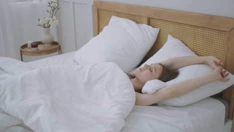 people waking up - young woman opens her eyes on a sunny morning. the girl lies in bed wakes up and sweetly stretches.