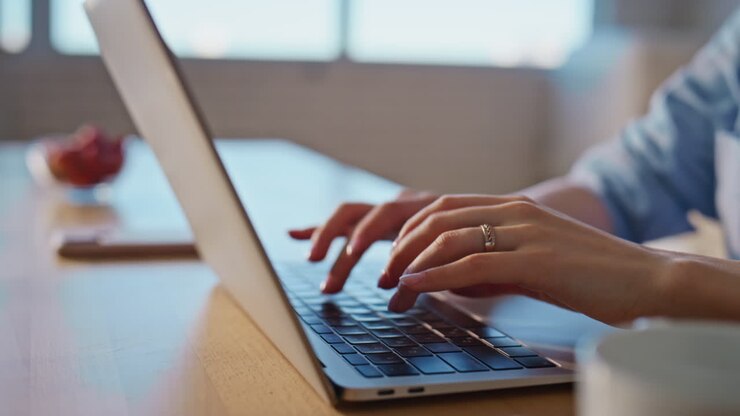 Frau tippt auf der Tastatur eines Laptops in der Küche, Nahaufnahme. Dame bei der Arbeit