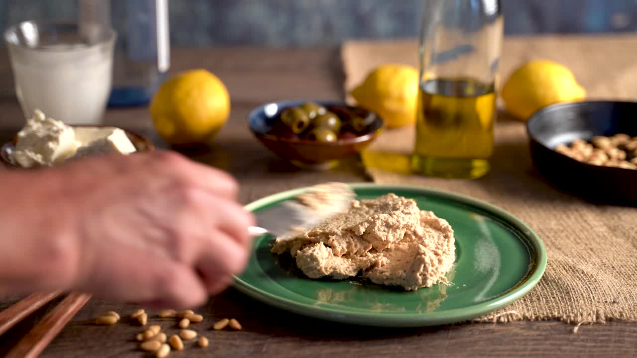 Clip lungo di una splendida composizione di cibo mediorientale mentre una mano spalma hummus su un piatto, versa olio d'oliva e sparge paprika