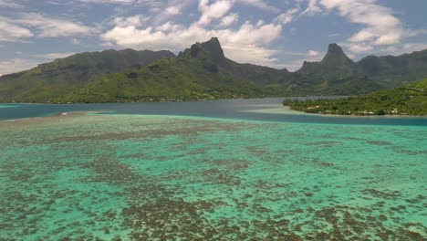 aerial establishing shot of mo'orea island, flying over the barrier reef and stunning mountains on background