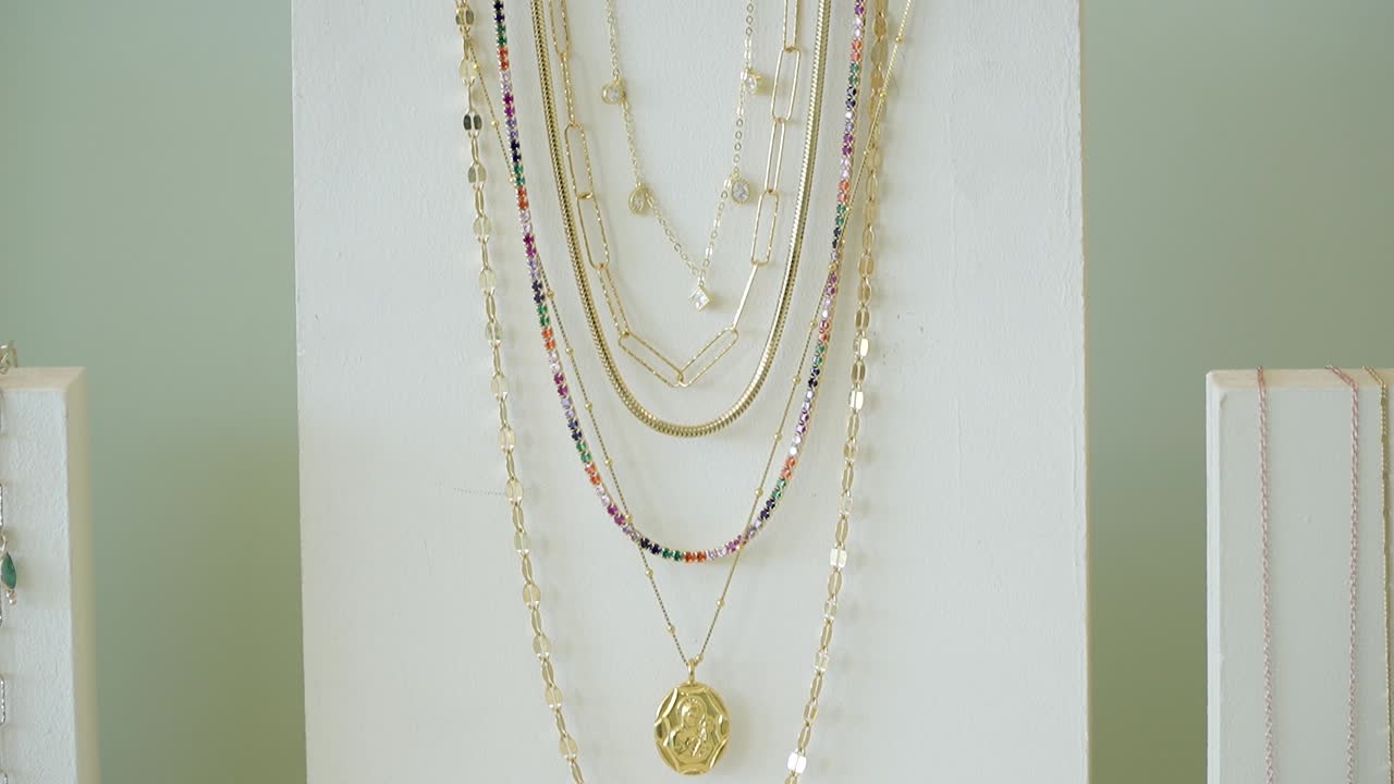 A collection of beautiful gold and colorful necklaces are showcased on a display stand in a local shop. The light enhances the shine of the jewelry pieces