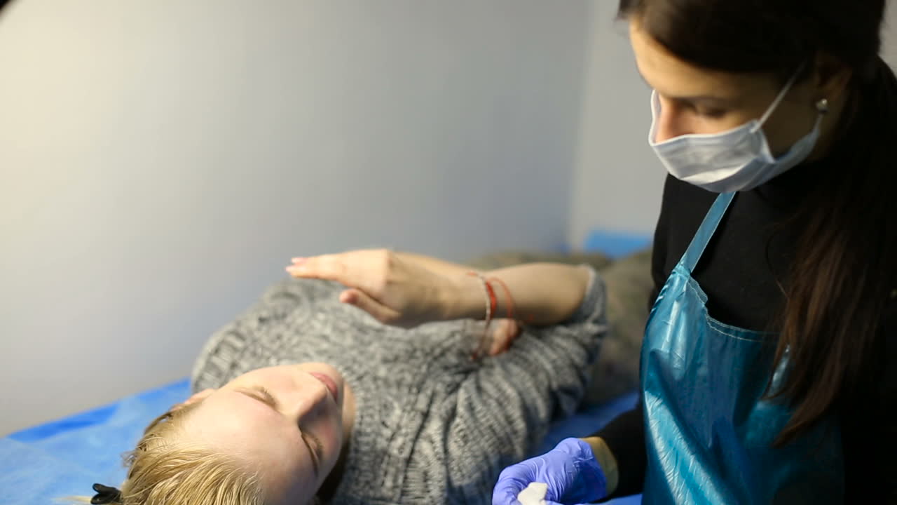 Woman getting eyebrow tattoo. Professional tattooist making eyebrow make up
