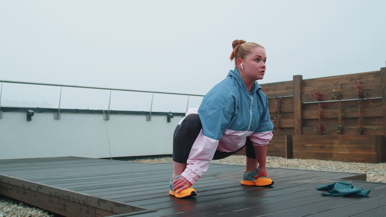mujer en forma deportiva en ropa deportiva azul rosa haciendo sentadillas yoga estiramiento ejercicio en el techo de la casa