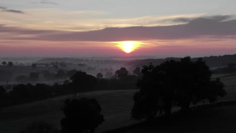 Drone-flying-over-deserted-fields-with-bright-sun-at-dusk-in-background,-Uchon-in-France