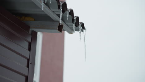 close-up of roof edge featuring frosted metal structure with icicles hanging down, highlighting frozen details and icy textures, set against a minimalistic winter sky with a blurred urban background