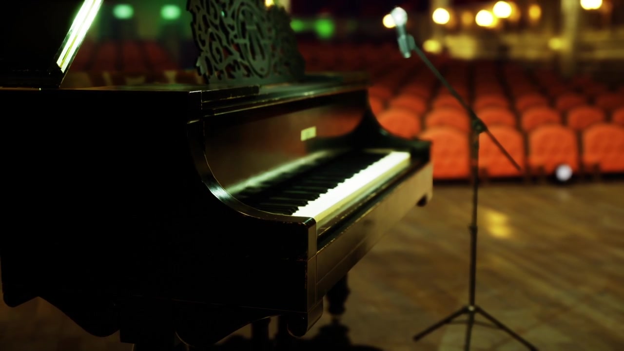 Primo piano di pianoforte e microfono con posti vuoti in un auditorium illuminato caldamente