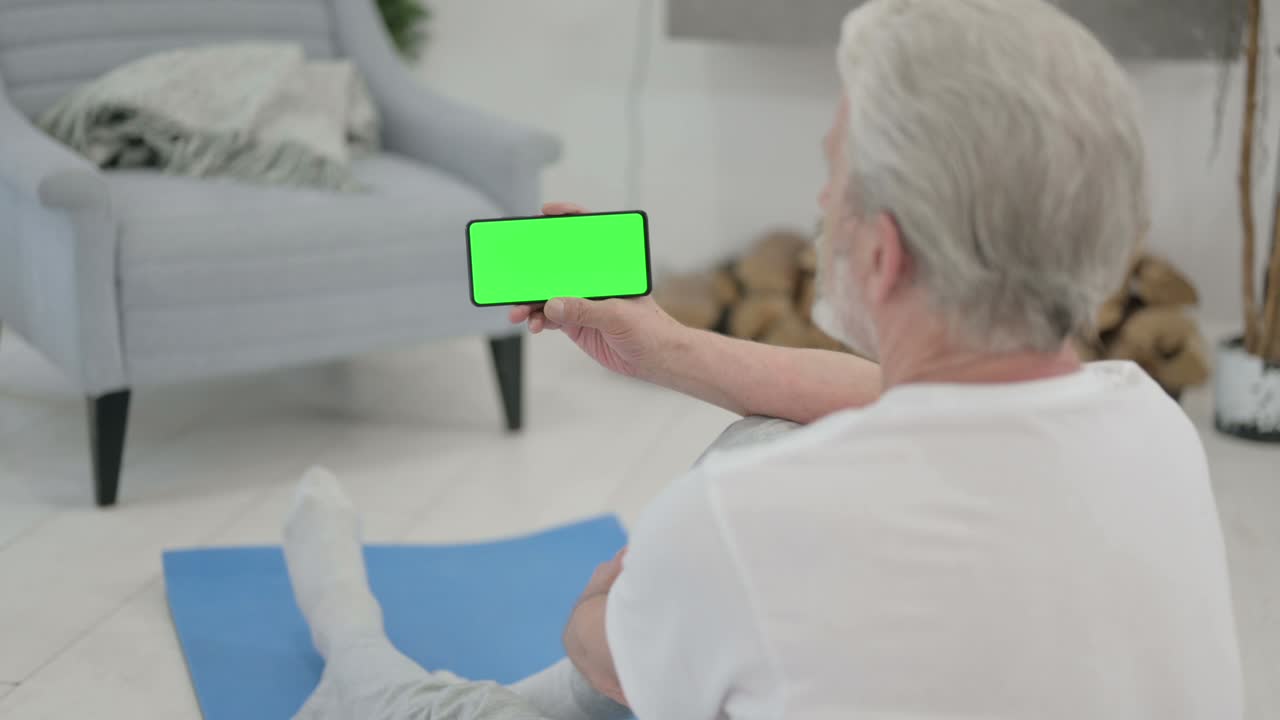 요가 매트 에 크로마 키 스크린 을 가진 스마트폰 을 보고 있는 노인 의 뒷면