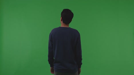 back view of asian refugee male shaking his head being sad due to the war while standing on the green screen background