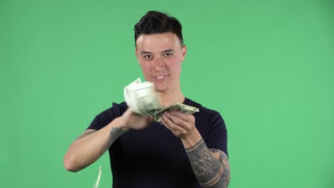 retrato de un joven guapo está mirando a la cámara y esparciendo dólares con expresión orgullosa y altiva, jactándose de una vida rica. pantalla verde