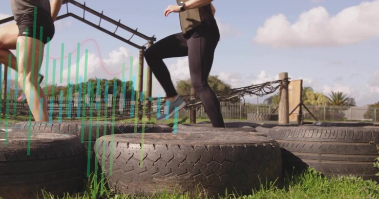 Two women initiating fitness exercise by placing right feet on first tire and hopping forward