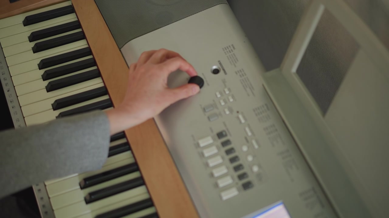 Mani sulla tastiera che regolano le impostazioni audio, musicista che sperimenta con preset e controlli a manopola, primo piano di tasti d'avorio e pannello di controllo, luce calma dello studio, pratica concentrata ed esplorazione tecnologica.