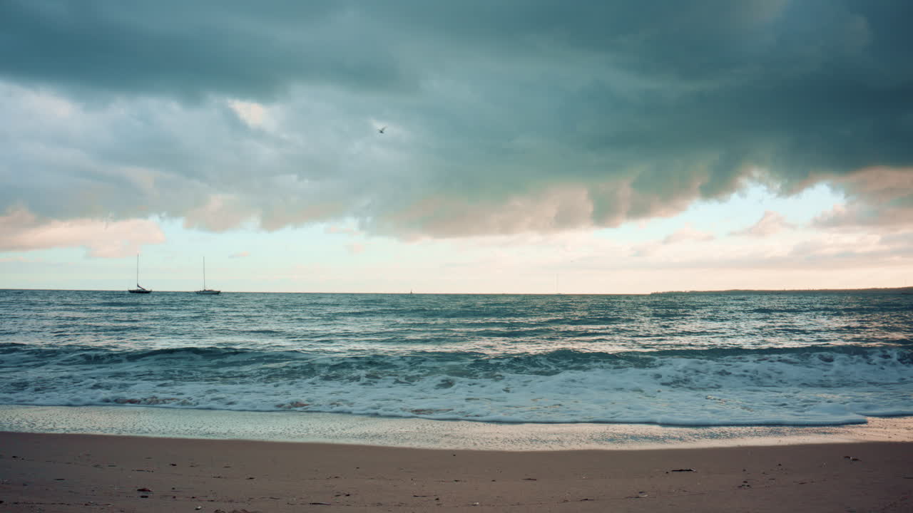 Wide shot of ocean waves crashing on the shore with moody clouds overhead
