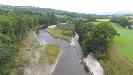 Drohnenaufnahmen,-Die-Langsam-über-Bäume-Und-Einen-Sich-Langsam-Bewegenden-Lazy-River-Und-Eine-Flussinsel-Mit-Freiliegendem-Flussbett-Und-Vegetation-Im-Seengebiet-Fliegen,-Großbritannien