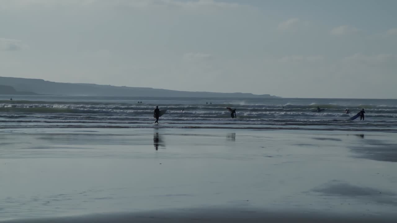 Surfers walking into the water and riding their surfboards, beautiful waves rolling in. Surfers defy the cold on a winter day and still go surfing at Lahinch, Ireland.