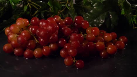 uvas rojas sin semillas sobre una superficie negra y húmeda