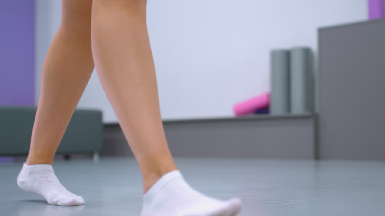 색 발목 양말을 입은 다리가 밝은 피트니스 스튜디오에서 요가 매트를 향해 고, 거울은 사람이 매트를 움직일 때 주변을 반영합니다.