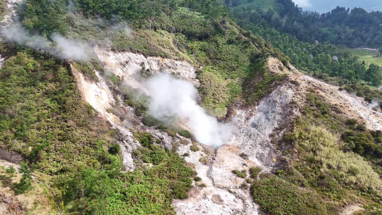 Aerial shot of a geothermal sulfur field with smoke rising from volcanic vents in a green mountain area