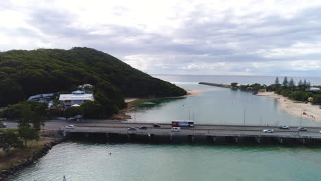 Aerial-view-of-drone-pulling-away-from-bridge,-revealing-a-group-of-paddle-boards-enjoying-the-beautiful-clear-water-at-Tallebudgera-Creek-QLD-Australia-with-Burleigh-Hill-in-the-background