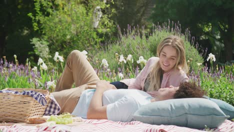 Happy-diverse-couple-having-picnic-in-garden-on-sunny-day