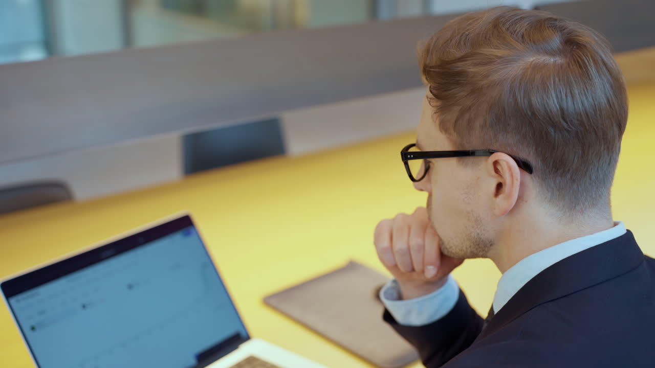 hombre de negocios reflexivo mirando el monitor de la computadora portátil. pesebre serio resolviendo problemas trabajando en un portátil moderno en el lugar de trabajo - vista trasera de primer plano